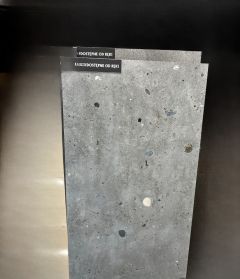 Dwie płytki imitujące beton na beżowym tle Płytka znadująca się z przodu imituje beton z rozmieszczonymi na jego powierzchni kamykami